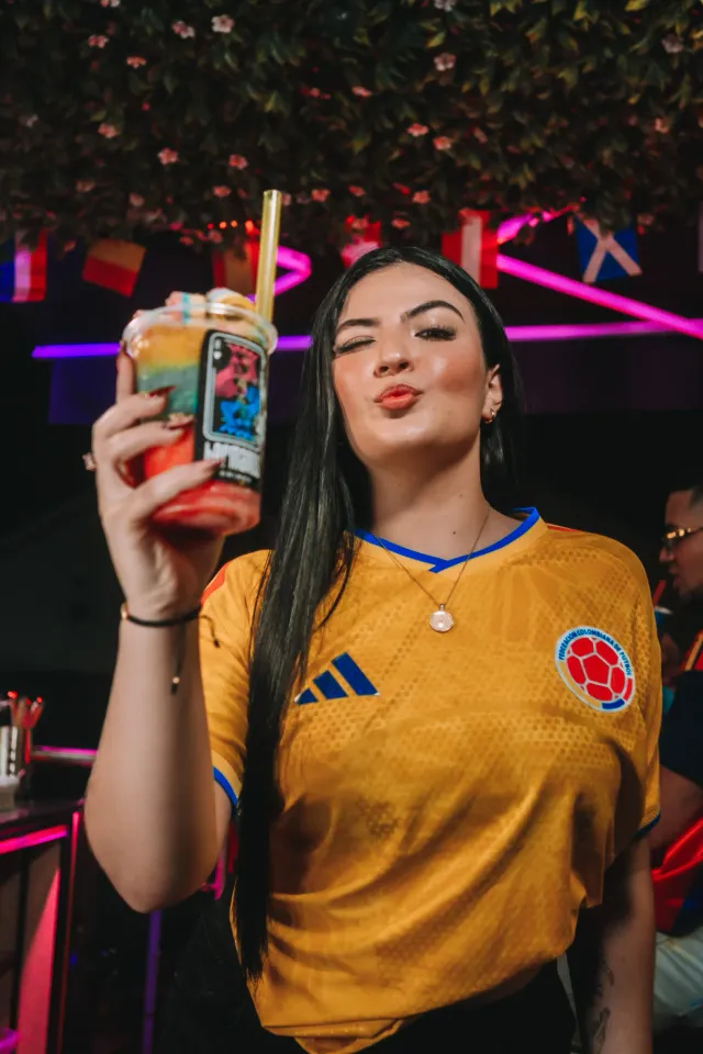 Chica con la camiseta de la selección Colombia levanta un granizado de capas de colores con pitillo dorado
